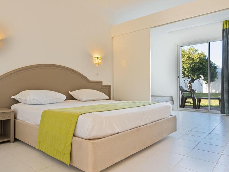Modern hotel room with double bed and access to a terrace overlooking trees.
