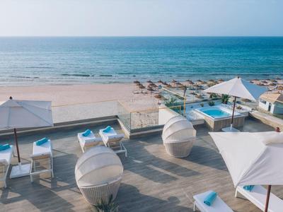 Strand mit blauem Meer, Sand, weißen Sonnenschirmen und modernen Liegen auf einer Holzterrasse.
