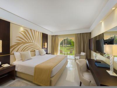 Chambre d'hôtel lumineuse avec grand lit, bureau, balcon et vue sur le jardin.