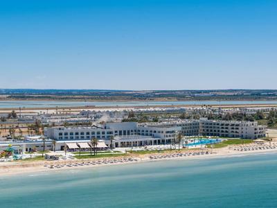 Strandhotel mit Pool, Sandstrand und ruhigem blauem Meer unter klarem Himmel.