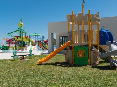 Kinder-Spielplatz mit bunten Rutschen, Türmen und Klettergerüsten auf grünem Rasen bei klarem Himmel.