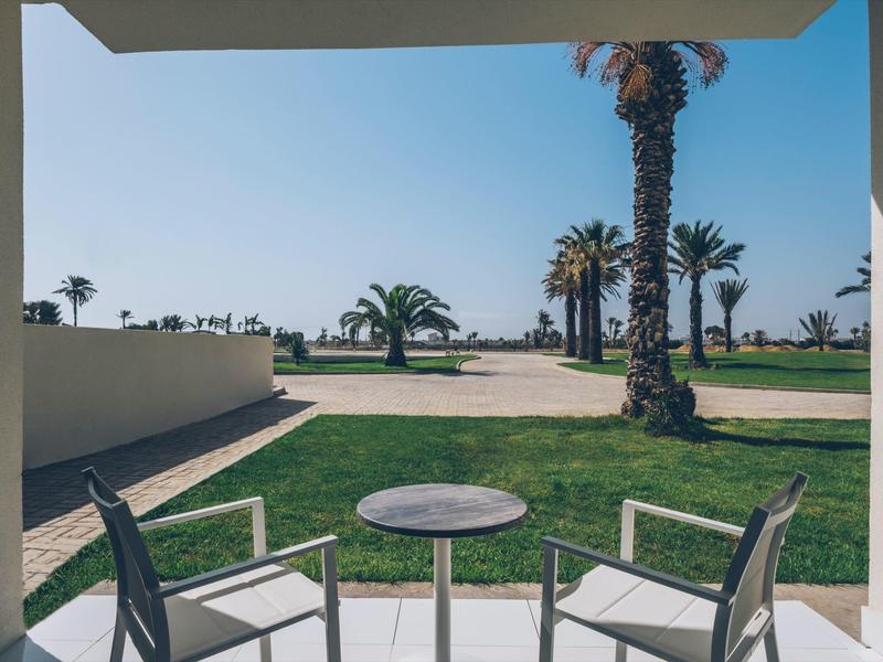 Terrasse avec deux chaises et une table, vue sur des palmiers et la mer au loin.