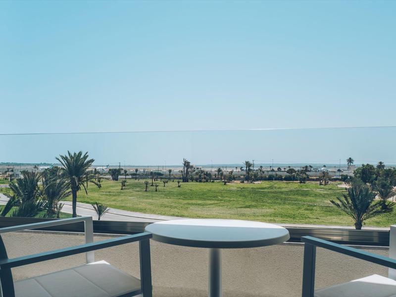 Balcon avec table et chaises surplombant un terrain de golf et des palmiers.