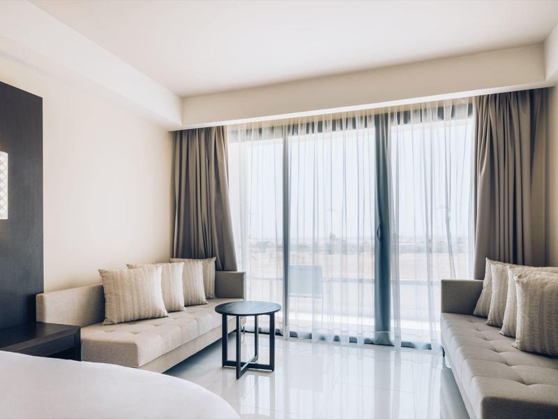 Chambre d'hôtel lumineuse avec deux canapés, grande fenêtre et décoration minimaliste.