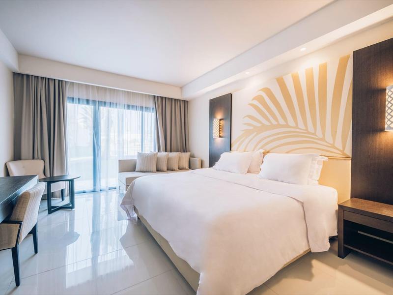 Chambre d'hôtel lumineuse avec grand lit, lumière naturelle et meubles modernes.