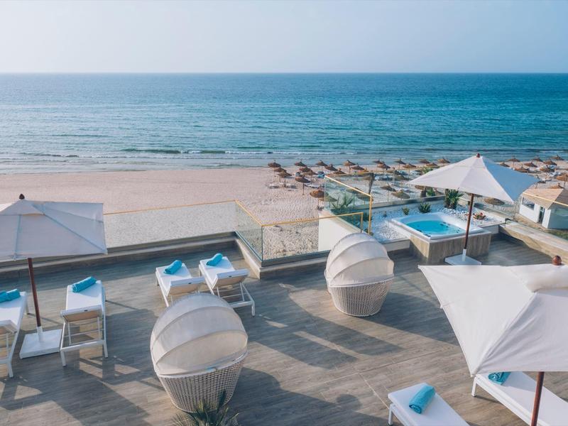 Vue sur la mer depuis une terrasse de plage avec parasols et meubles lounge.