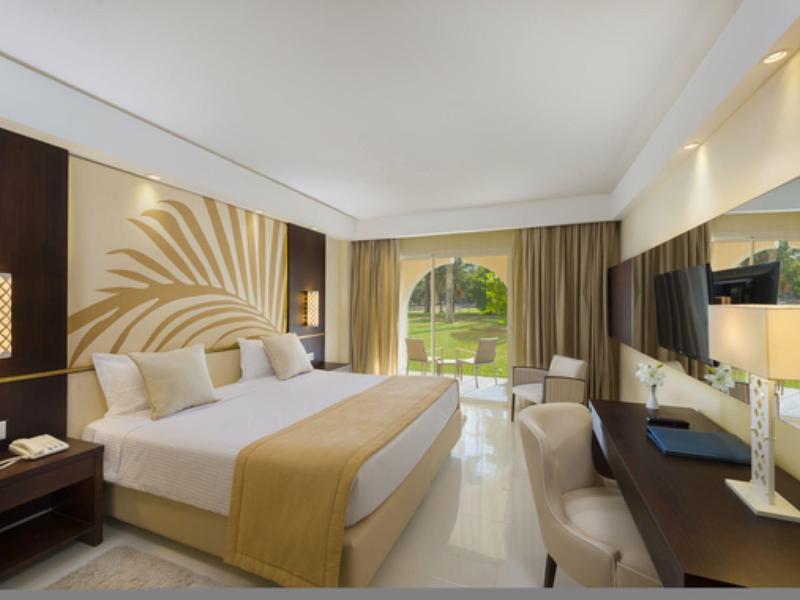 Chambre d'hôtel lumineuse avec grand lit, bureau, balcon et vue sur le jardin.