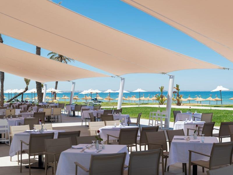 Terrasse de restaurant en plein air avec vue sur la mer et parasols blancs.