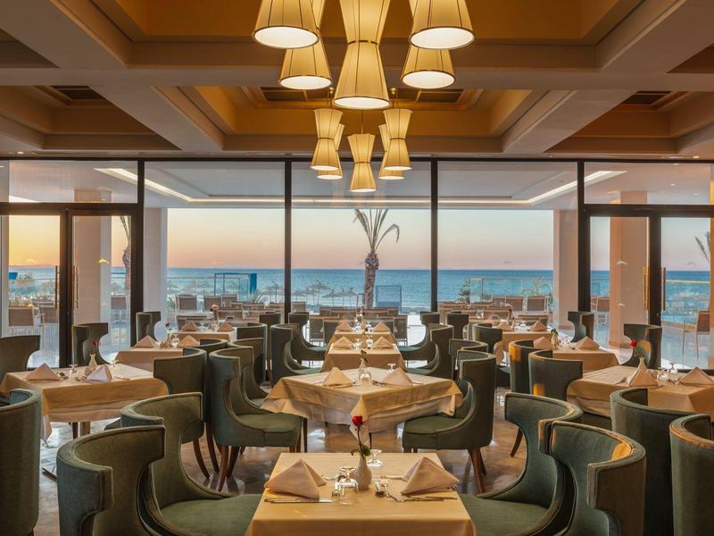 Restaurant élégant avec tables en bois, chaises confortables et vue sur la mer au coucher du soleil.