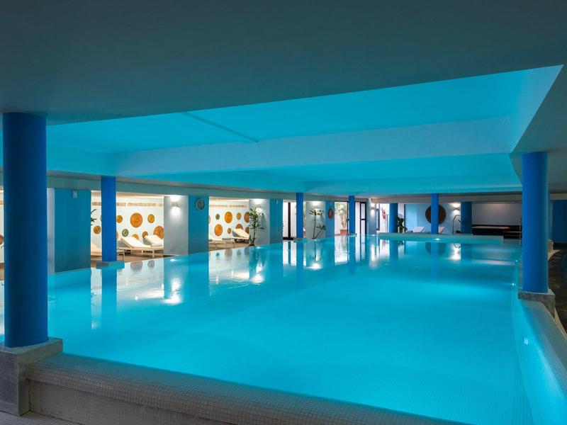 Piscine intérieure chauffée avec éclairage bleu et fenêtres vitrées ornées de motifs ronds
