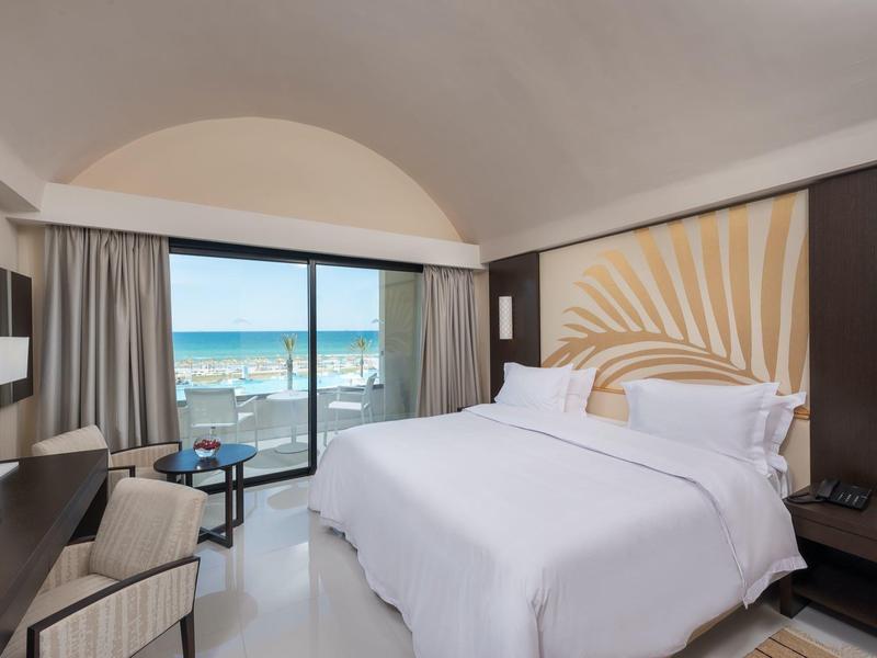 Chambre d'hôtel lumineuse avec grand lit et balcon vue mer.