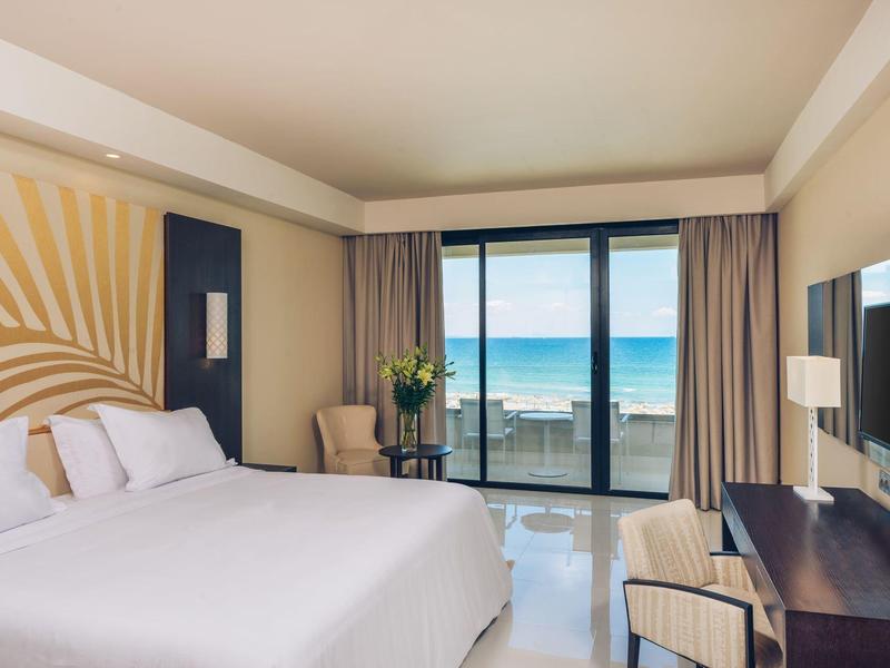 Chambre d'hôtel moderne avec grand lit et vue sur la mer par des fenêtres du sol au plafond