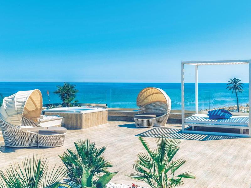 Terrasse luxueuse avec sièges ronds, lit à ciel ouvert et vue sur la mer.