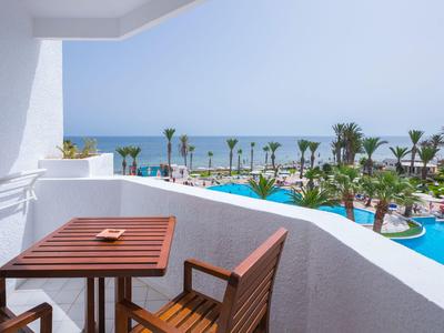 Balkon mit Holztisch und Stuhl mit Blick auf Poolbereich und Meer im Hintergrund.