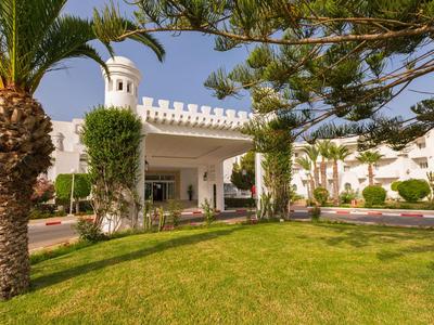 Hotelgebäude mit weißer Fassade, umgeben von grünen Palmen und einem gepflegten Rasen.