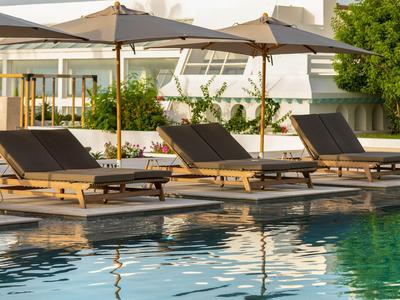 Mehrere Liegestühle mit Sonnenschirmen an einem klaren Pool in einer Hotelanlage.