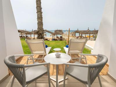 Blick von einer Terrasse mit Stühlen und Tisch auf einen Garten und das Meer dahinter.
