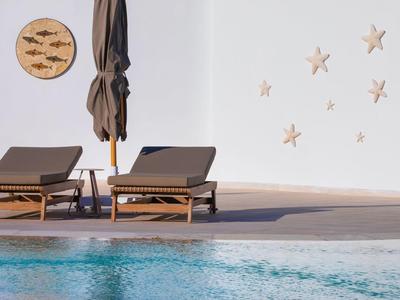 Zwei braune Liegen am Pool mit geschlossenem Sonnenschirm, Wand mit Fischen und Seesternen dekoriert.