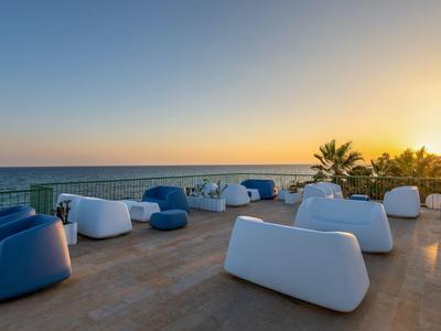 Terrasse mit modernen weißen und blauen Sitzmöbeln neben Meer bei Sonnenuntergang.