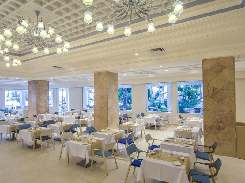 Eleganter, heller Speisesaal mit weißen Tischen und blauen Stühlen in einem Hotel.