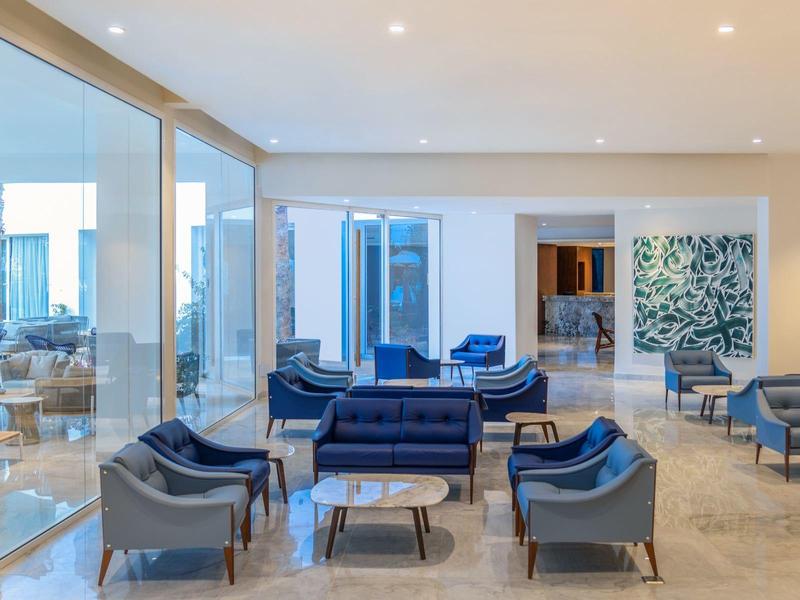 Moderner, heller Wohnraum mit blauen Sesseln, großen Fenstern und hellem Bodenbelag.