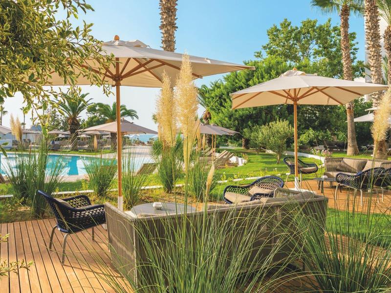 Gemütlicher Außenbereich mit Sonnenschirmen, Liegestühlen, grünem Rasen und Pool bei Sonnenschein.