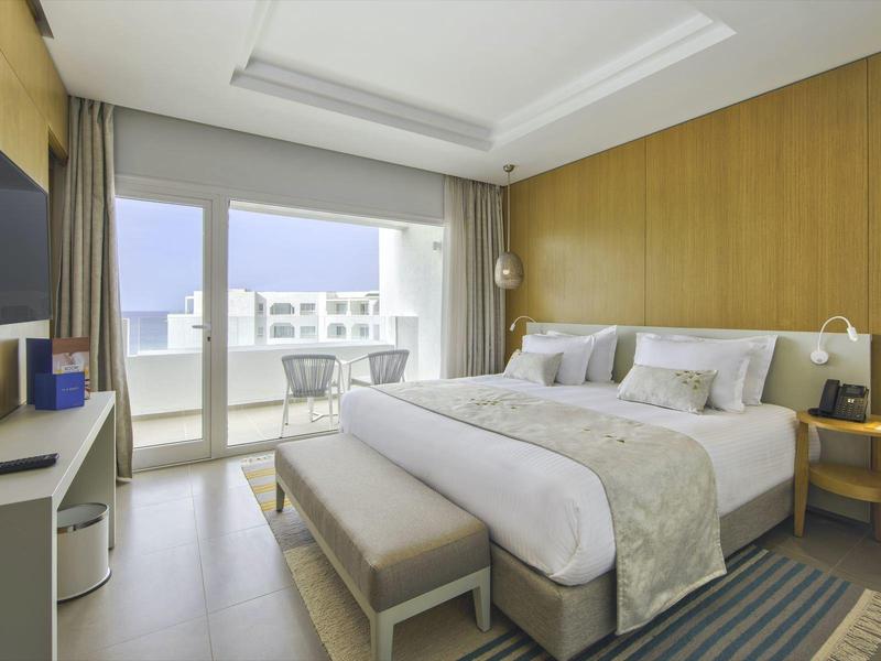 Modernes Schlafzimmer mit großem Bett, Holzvertäfelung, Balkon und hellen, neutralen Farbtönen.