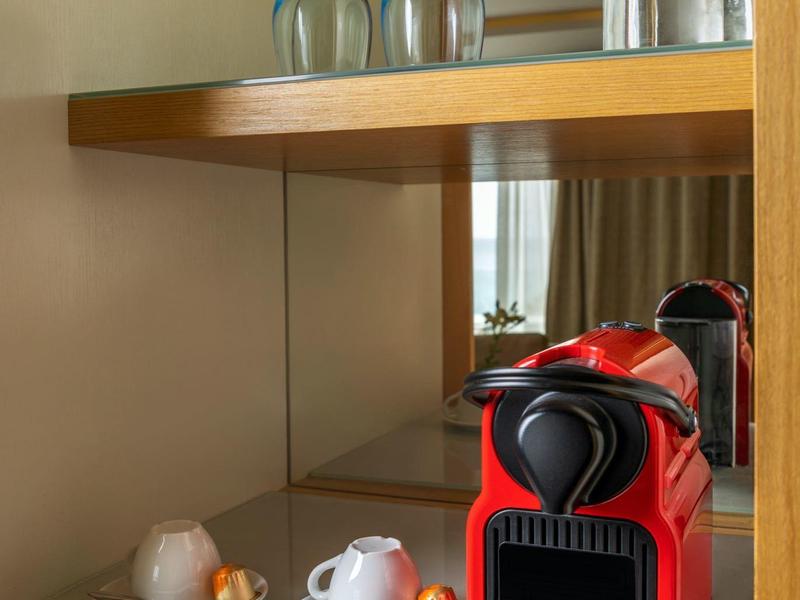 Rote Kaffeemaschine mit Tassen und Gläsern auf einem weißen Regal in einem Holzmöbel.