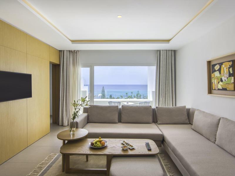 Moderner Wohnraum mit L-förmigem grauem Sofa, Holztisch, Fenster mit Meerblick und Wandbild.