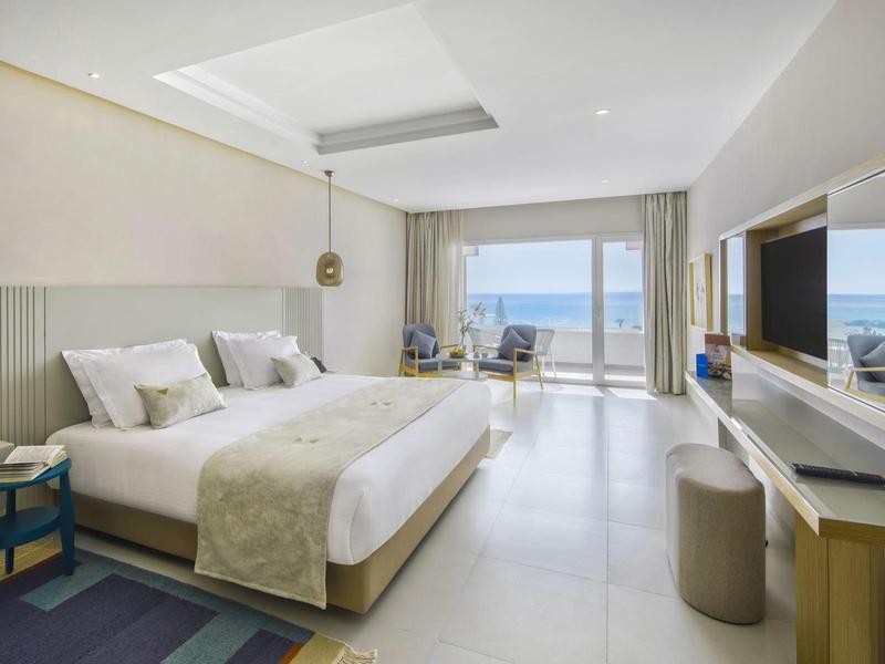 Modernes Schlafzimmer mit großem Bett, hellen Wänden, Meerblick und minimalistischer Einrichtung.