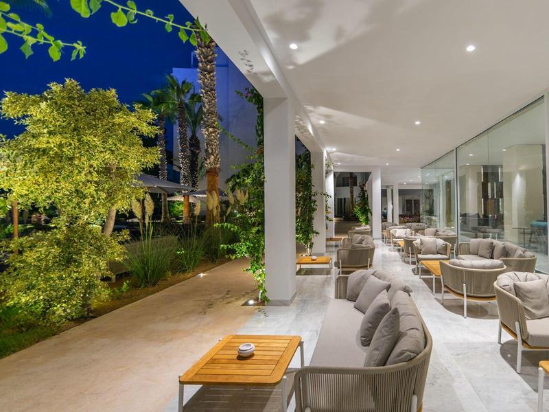 Moderner Außenbereich mit gemütlichen Sesseln, gläserner Wand und beleuchtetem Garten bei Nacht.