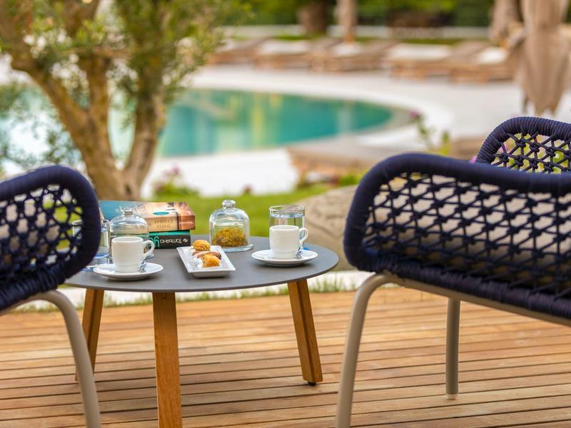 Gemütliche Sitzgruppe mit schwarzem Netzstuhl und Tisch mit Kaffee und Snacks am Pool.