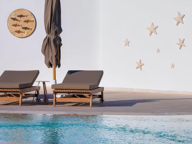 Zwei braune Liegen am Pool mit geschlossenem Sonnenschirm, Wand mit Fischen und Seesternen dekoriert.