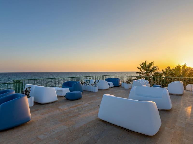 Terrasse mit modernen weißen und blauen Sitzmöbeln neben Meer bei Sonnenuntergang.