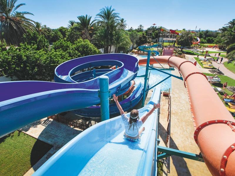 Personne glisse sur un toboggan aquatique bleu dans un parc de vacances tropical.