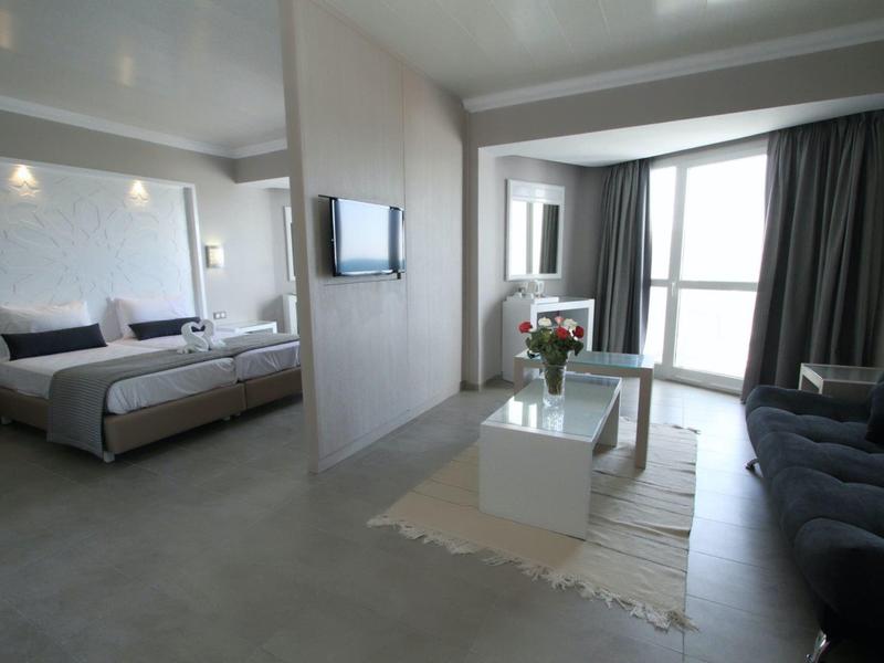 Chambre d'hôtel moderne avec lit, canapé et grande fenêtre avec rideaux.