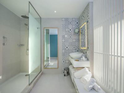 Moderní koupelna se skleněným sprchovým koutem, umyvadlem a vzorovanými dlaždicemi na stěně.