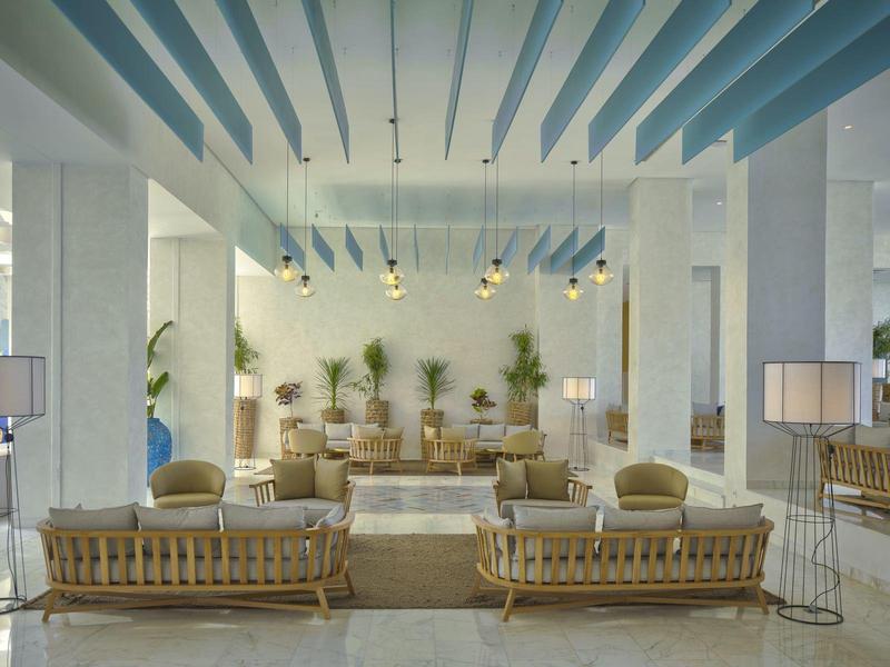 Světlý hotelový salonek s moderním dřevěným nábytkem a modrými stropními detaily.