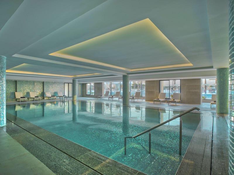 Vnitřní bazén s moderním osvětlením a velkými okny v hotelu.