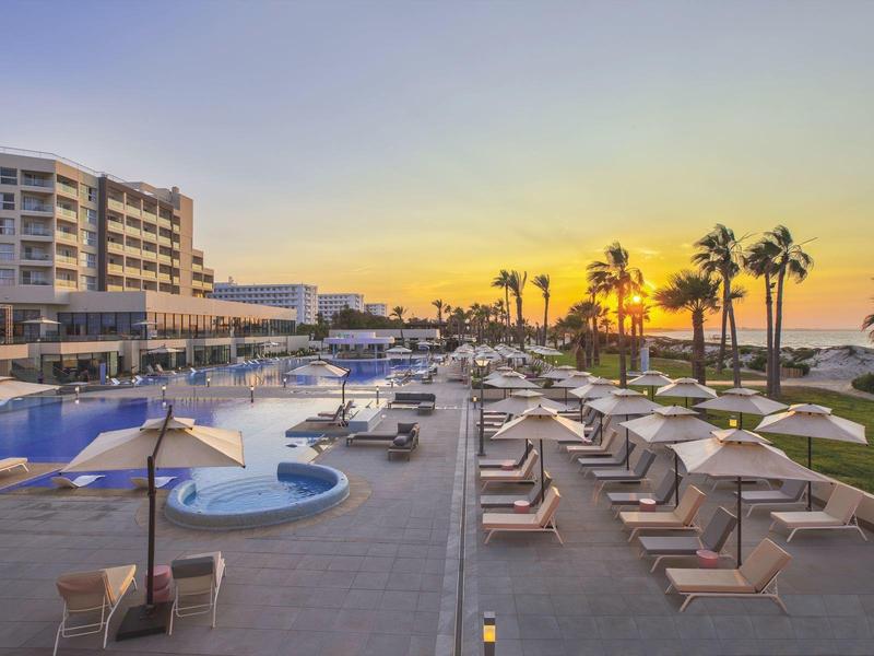 Luxusní hotel s bazénem, lehátky a palmami při západu slunce u moře