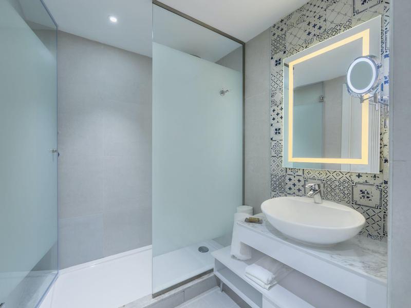 Moderní koupelna s bezbariérovým sprchovým koutem, osvětleným zrcadlem a bílým umyvadlem.