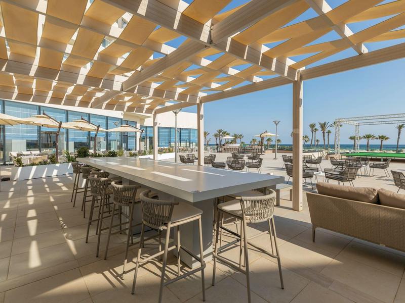 Otevřená lounge s posezením pod moderní pergolou s výhledem na moře.