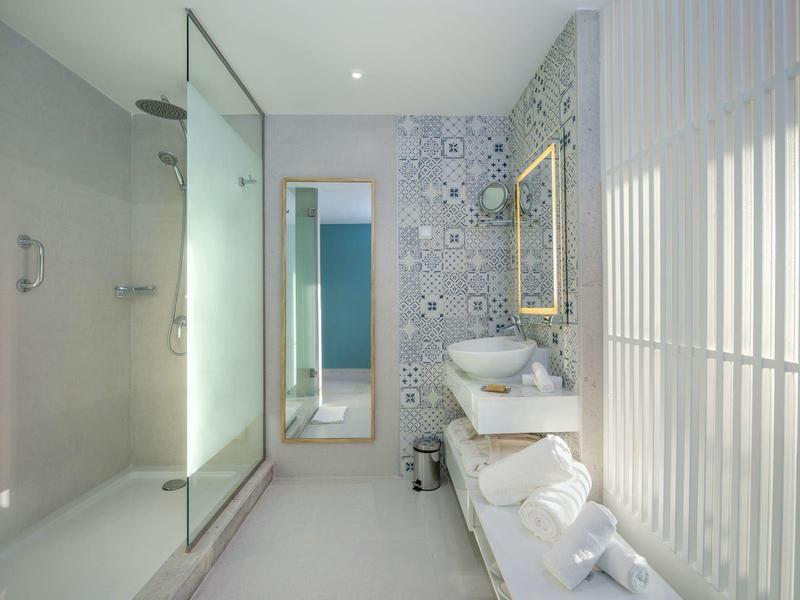 Moderní koupelna se skleněným sprchovým koutem, umyvadlem a vzorovanými dlaždicemi na stěně.