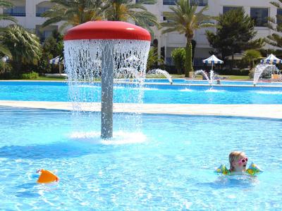 Kinder planschen in einem Pool mit einem roten Wasserspiel in einer Hotelanlage.
