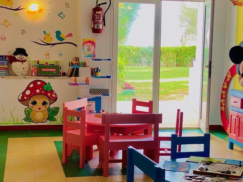 Kleurrijke kinderspeelruimte met tafels, stoelen en wanddecoraties in een lichte kamer.