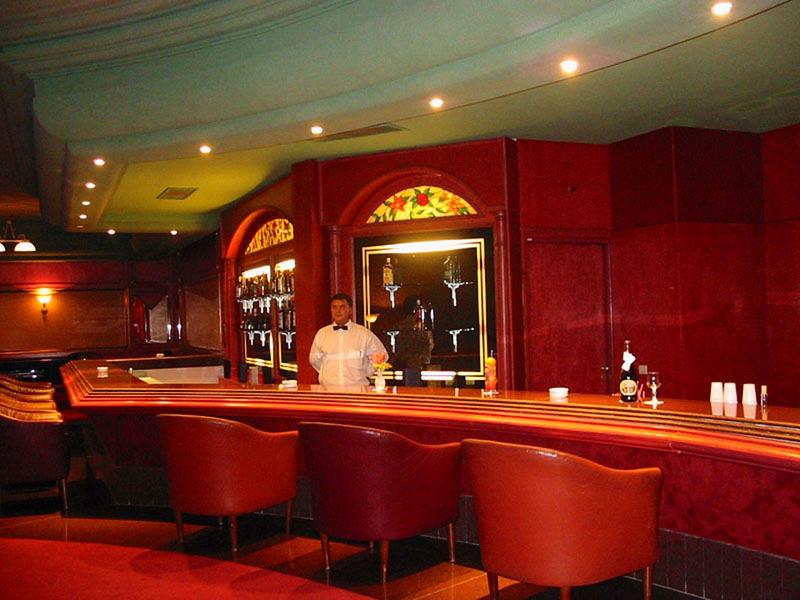 Elegante hotelbar met rode stoelen, houten wanden en barkeeper achter de bar.