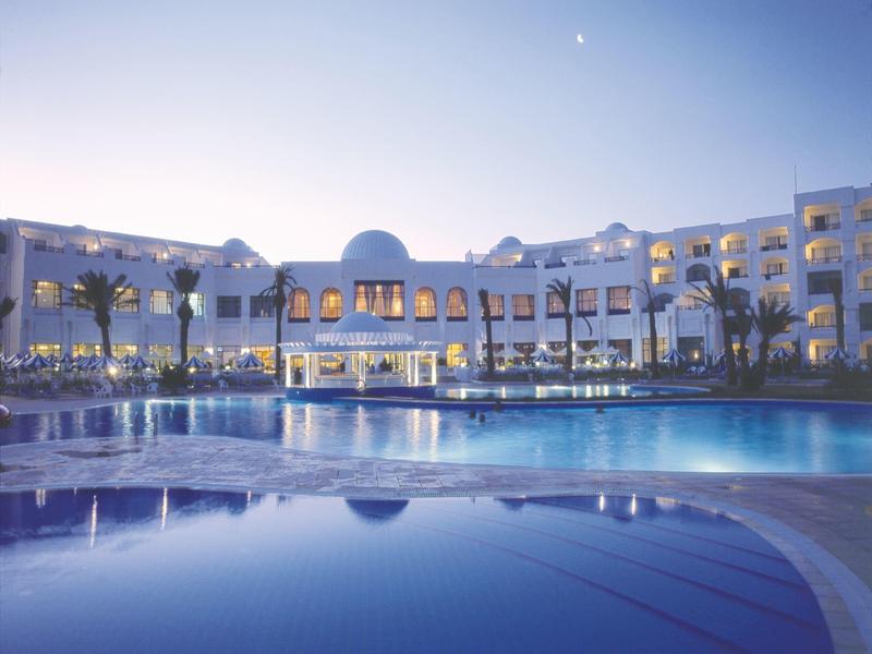 Luxe hotel met verlicht zwembad en palmbomen bij schemering onder heldere lucht