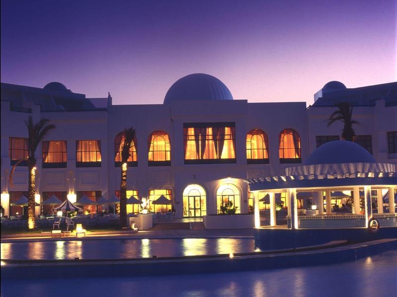 Hotelgebouw bij schemering met verlichte ramen en zwembad op de voorgrond.