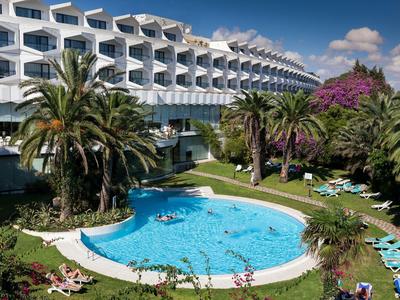 Modernes Hotel mit einem runden Außenpool, umgeben von Palmen und Liegestühlen