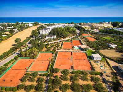 Luchtfoto van tennisbanen met rode gravel nabij een kustplaats met de zee op de achtergrond.